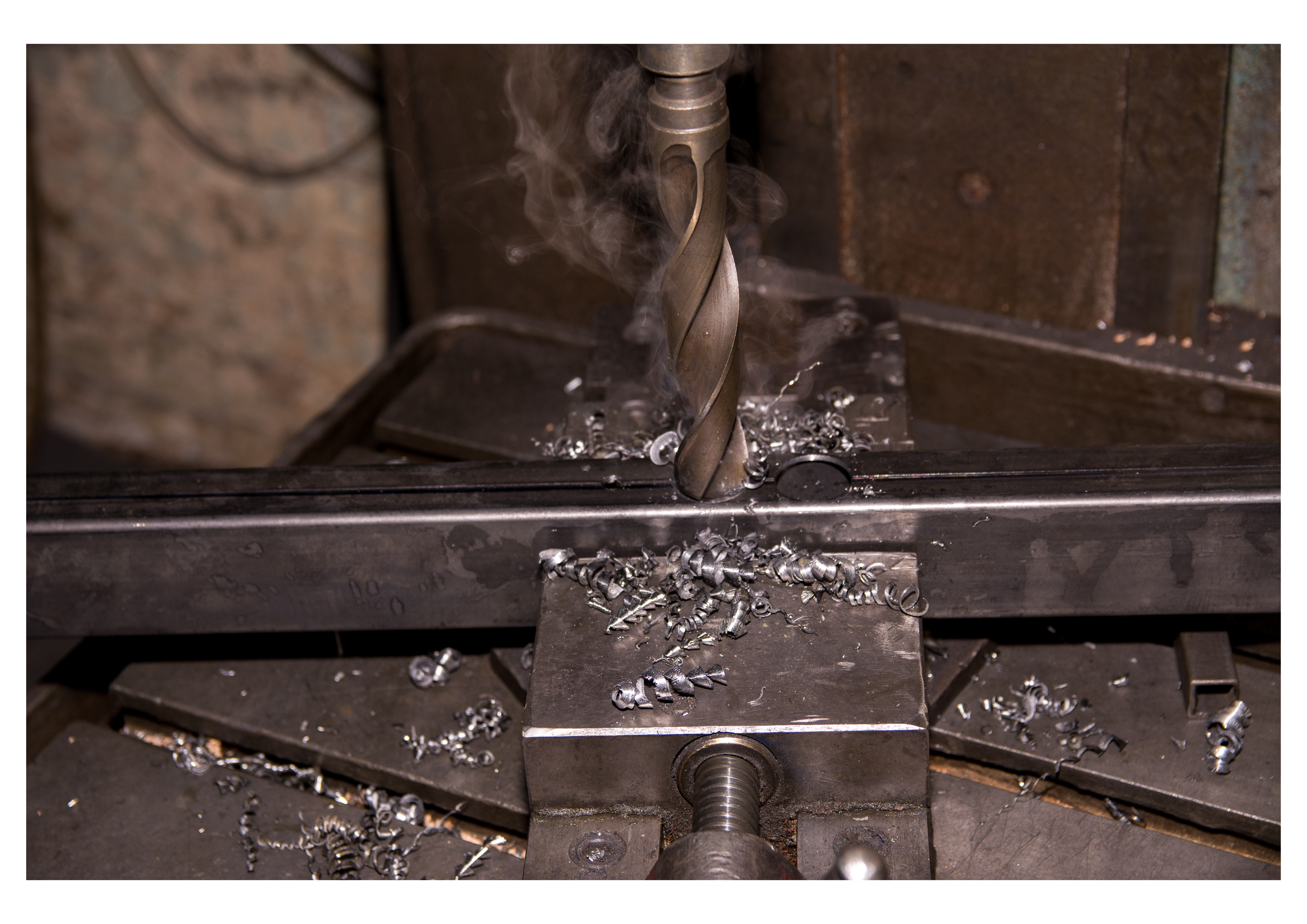 A pillar drill boring a steel section clamped in a vice, with chips and smoke